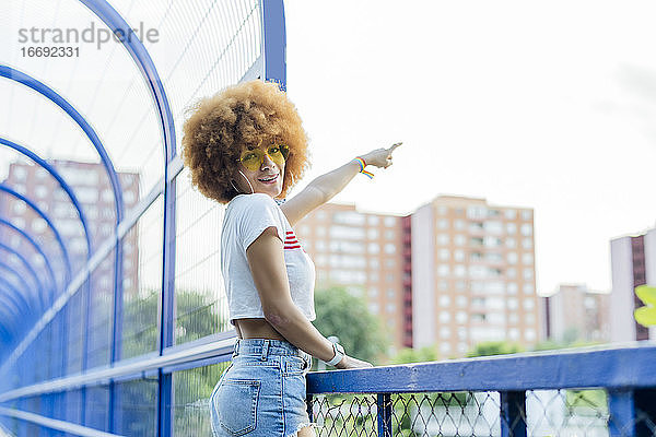 Frau mit Afro-Haar  die auf eine Brücke zeigt