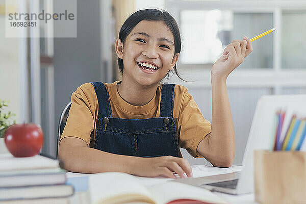 Glückliches asiatisches Mädchen lernt online zu Hause