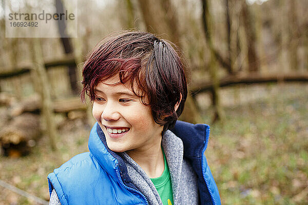 Ein lächelnder Junge schaut zur Seite  während er im Frühling im Wald steht