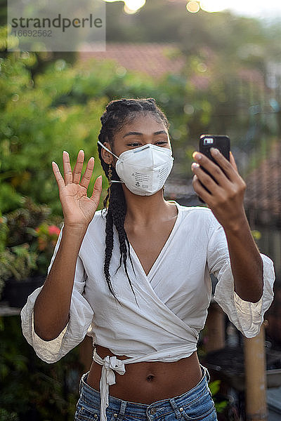 Junge schwarze Frau mit Gesichtsmaske bei einem Videogespräch