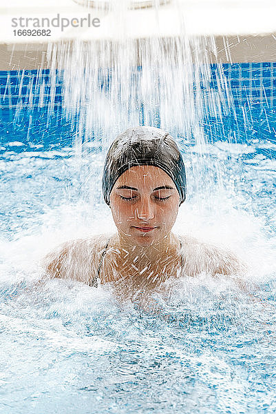 Junges hübsches Mädchen  Augen geschlossen  entspannt unter einem Wasserfall in einem Spa