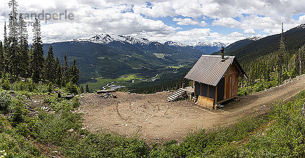 Kleine Hütte in der Nähe einer Holzfällerstraße vor verschneiten Bergen und bewölktem Himmel im Hochland von British Columbia  Kanada