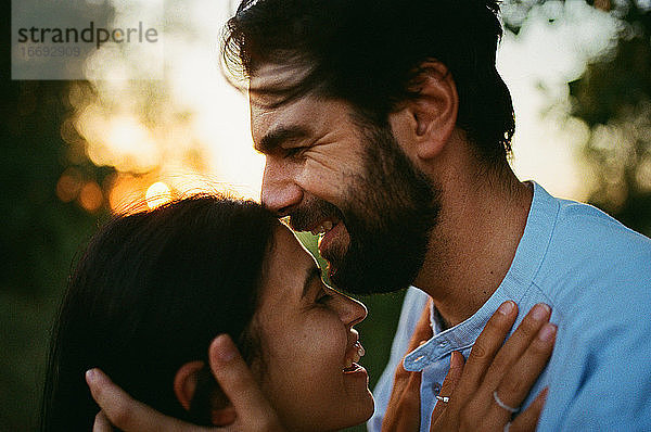 Mann lacht und küsst Frau im Freien bei Sonnenuntergang