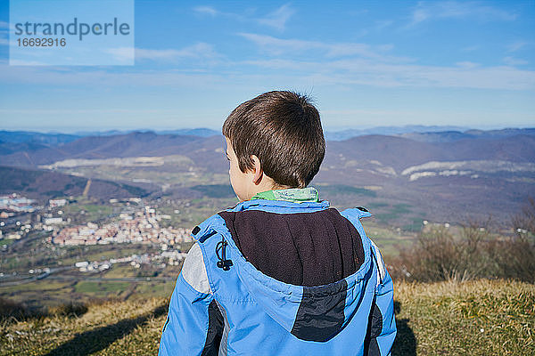 Junge auf dem Rücken schaut mit blauem Mantel in die Herbstlandschaft