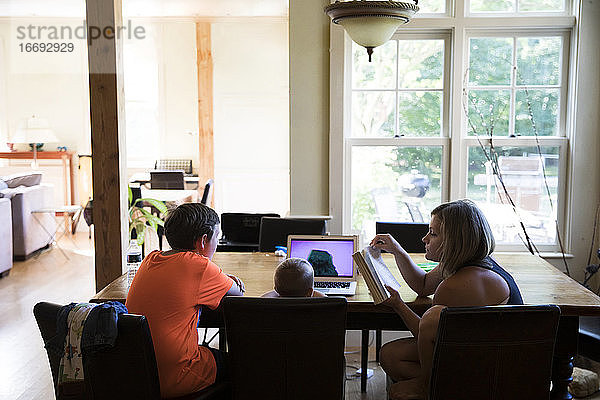 Mutter und Kleinkind Sohn Watching Laptop sitzen mit Teenager-Cousin am Tisch