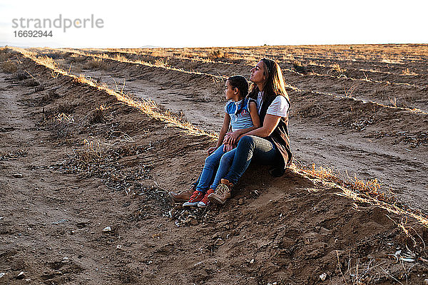 eine Mutter sitzt auf dem Feld und spielt mit ihren Töchtern