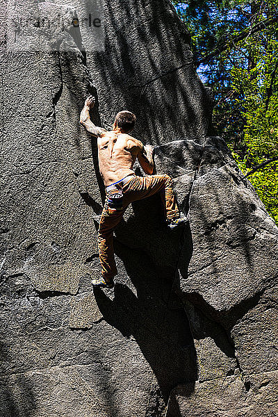 Hemdsärmeliger  fitter Kletterer auf dem Weg zum Gipfel des Felsblocks