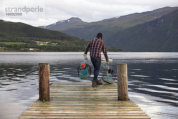 Ein Fischer  der gerade dabei ist  einige Krabbenreusen von einem Dock in Norwegen zu werfen