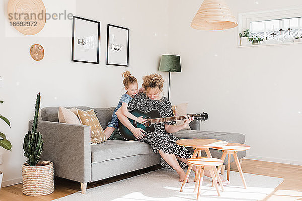 Mutter und Tochter spielen zu Hause gemeinsam Gitarre