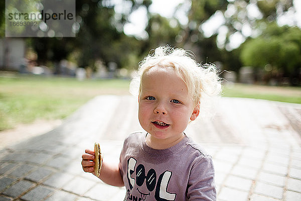 Nahaufnahme eines zweijährigen Kindes  das einen Snack im Park zu sich nimmt