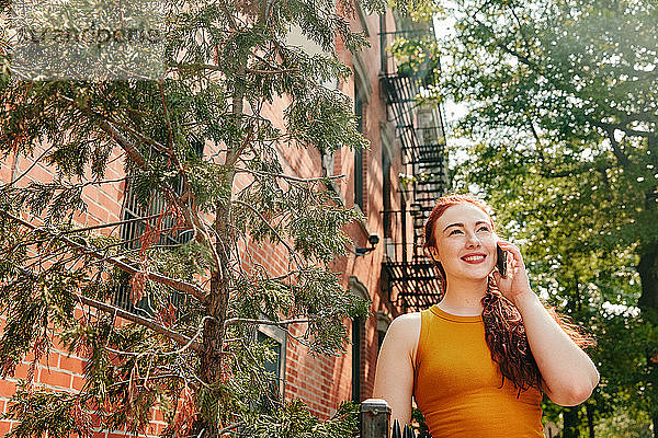 Junge Frau telefoniert fröhlich im Freien auf der Straße in Brooklyn.