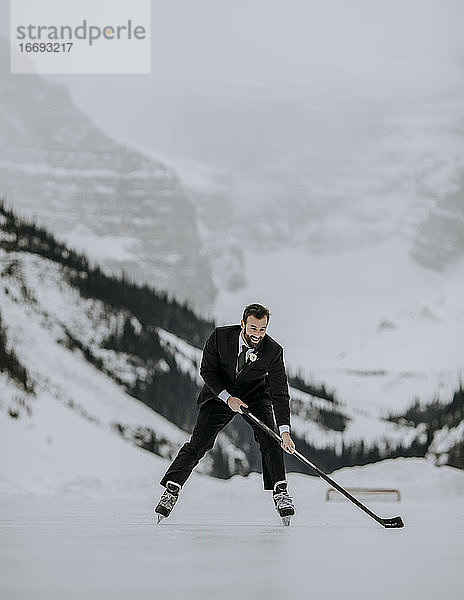 Frisch verheirateter Bräutigam fährt Schlittschuh mit Eishockeyschläger auf dem Lake Louise  Alberta