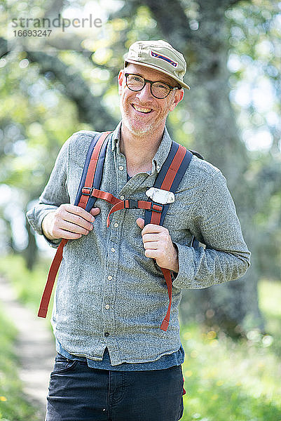 Porträt eines lächelnden Wanderers mit Hut  Brille und Rucksack im Freien