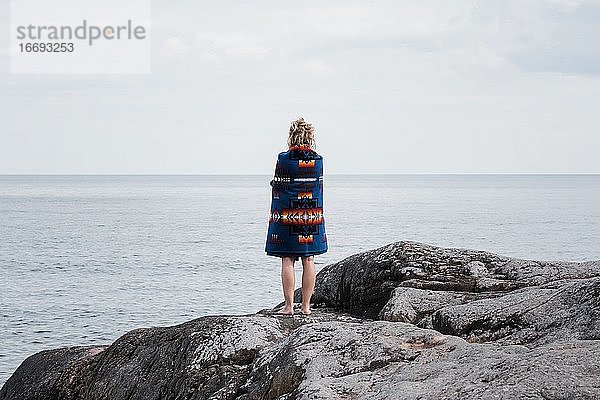 Frau auf Felsen stehend  eingewickelt in eine Pendleton-Decke in Schweden