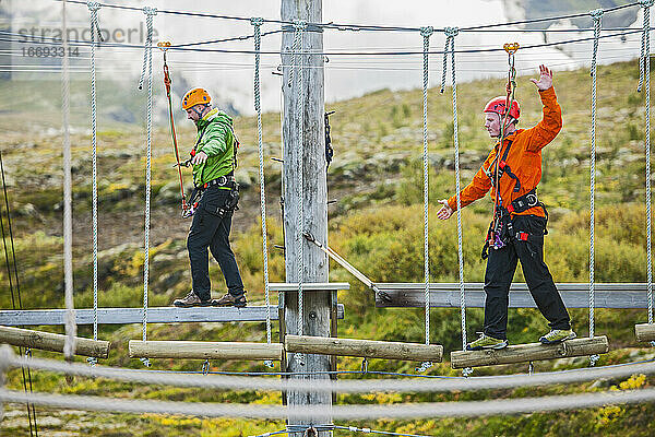 Zwei Männer balancieren auf einem Hochseilgarten in Island