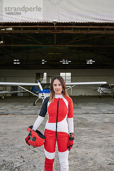 Junge Fallschirmspringerin in einem Hangar mit einem Flugzeug hinter ihr