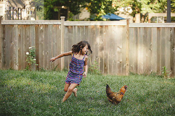 Ein glückliches Kind spielt barfuß mit einem Huhn in seinem Garten