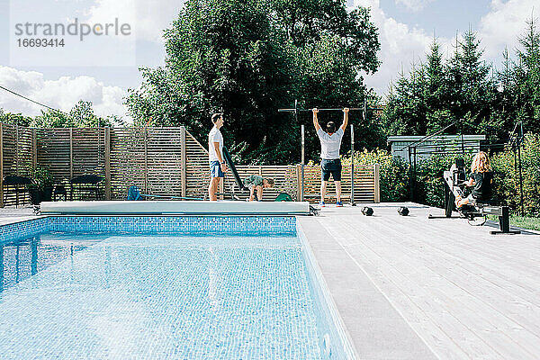 zwei Männer und ihre Kinder trainieren im heimischen Fitnessstudio am Pool