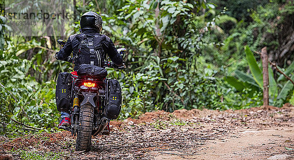 Frau fährt mit ihrem Scrambler-Motorrad durch den Wald