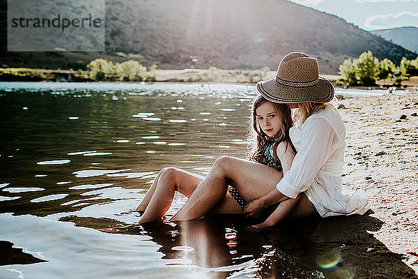 Mutter und Tochter sitzen ruhig im Wasser an einem Seeufer