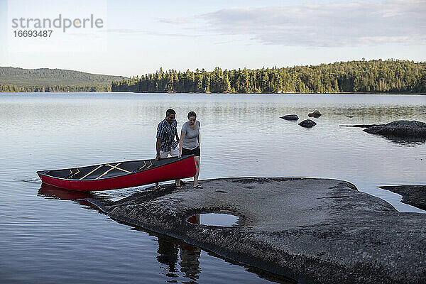 Afrikanischer Mann und weiße Frau ziehen Kanu auf einem Teich in Maine ans Ufer