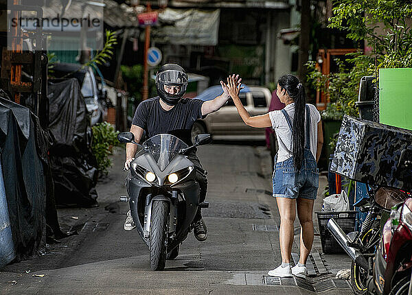 Motorradfahrer  der einer Frau in einer Seitengasse ein High Five gibt