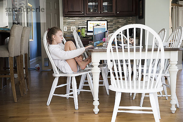 Junges Mädchen sitzt am Küchentisch und macht Schularbeiten am Laptop