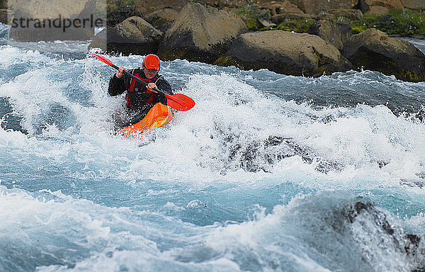 Ein Mann fährt mit seinem Wildwasserkajak auf einem isländischen Fluss