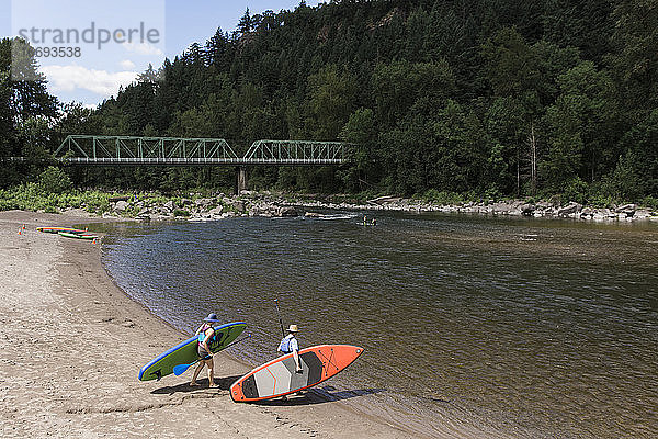 Ein junges Paar trägt Standup-Paddleboards zum Wasser in Oregon.