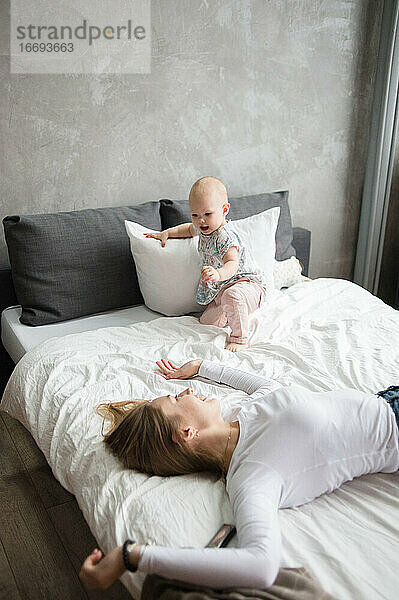 Junge Frau und kleines Mädchen liegen auf dem Bett und lächeln beim Spielen. Kindermädchen.