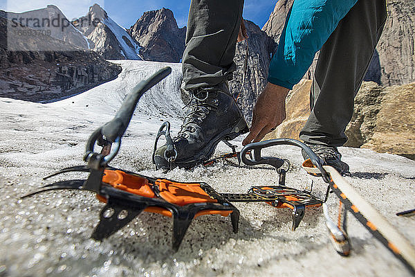 Bergsteiger schnallt auf dem Gletscher Steigeisen an seine Bergschuhe.