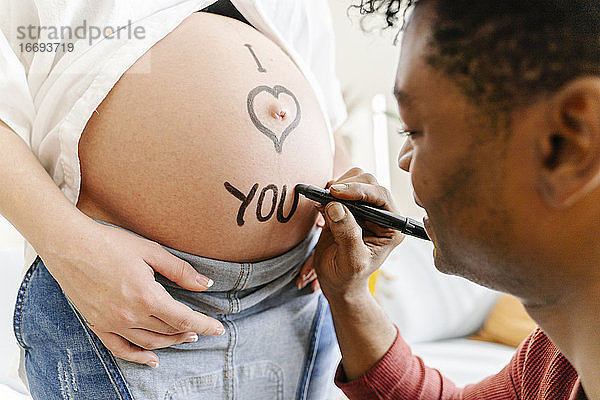 Ehemann zeichnet den Satz Ich liebe dich auf den Bauch seiner schwangeren Frau. Konzept der Elternschaft