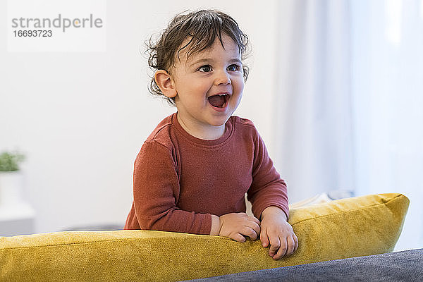 Fröhlicher Junge schaut weg  während er zu Hause auf dem Sofa steht