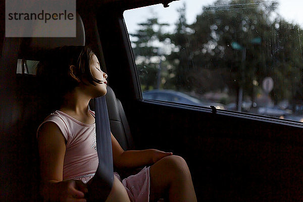 Ein hübsches  angeschnalltes kleines Mädchen schläft in der Dämmerung in einem Auto
