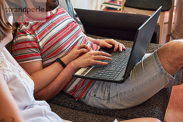 Junges Paar schaut auf ihren Computer  während sie sich an den Händen halten