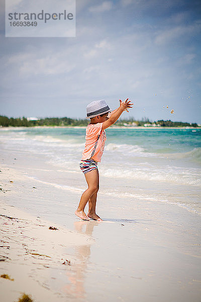 Kleiner Junge mit lockigem Haar wirft Sand an einem Strand in der Karibik