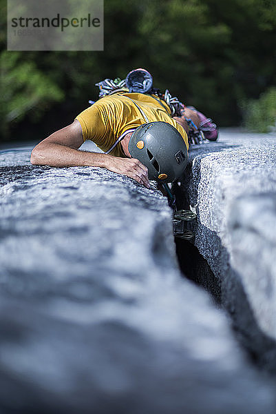 Mann platziert Sicherung beim Klettern eines breiten Risses auf Granit Squamish