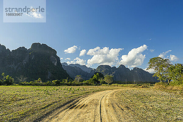 Schotterstraße in einem Bauernhof mit Kalksteinbergen im Hintergrund  Vang Vieng  Laos