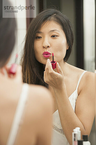 schöne Frau trägt Lippenstift auf  während sie in den Spiegel schaut