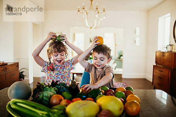Zwei glückliche Kinder spielen mit Obst und Gemüse in der Küche