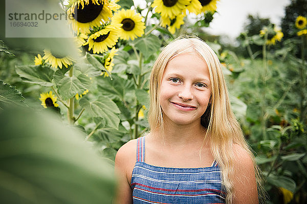 Junges Mädchen in Casual Blue Dress Standing in Sunflower Field Lächelnd