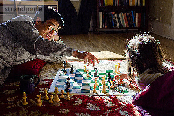 Ein lächelnder Vater und sein kleines Mädchen spielen Schach in einem hellen Lichtfleck