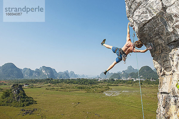 Männlicher Kletterer hängt seitlich an einem überhängenden Felsen in Yangshuo / China