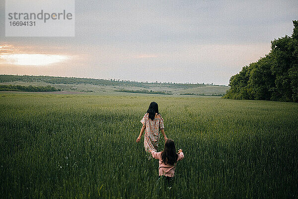 Mutter und Tochter spazieren in einem Feld bei Sonnenuntergang