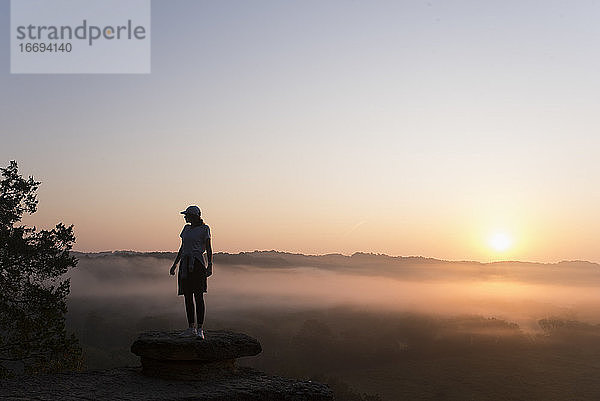 Silhouette eines Mädchens beim Wandern auf einem Berggipfel bei Sonnenaufgang