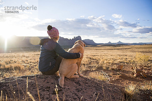 Eine Frau und ihr gelber Labrador genießen einen wunderschönen Sonnenuntergang in der Wüste.