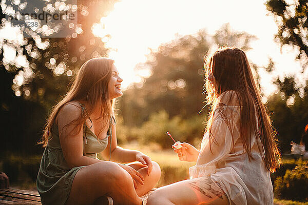 Glückliche Freundinnen sitzen im Sommer bei Sonnenuntergang im Park