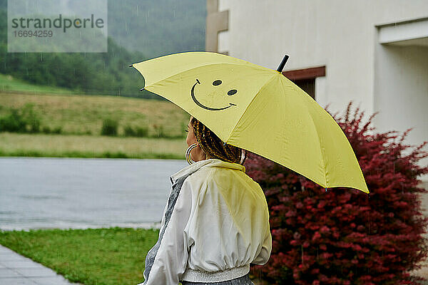 Rückenansicht eines Mädchens  das sich mit einem gelben Regenschirm vor dem Regen schützt