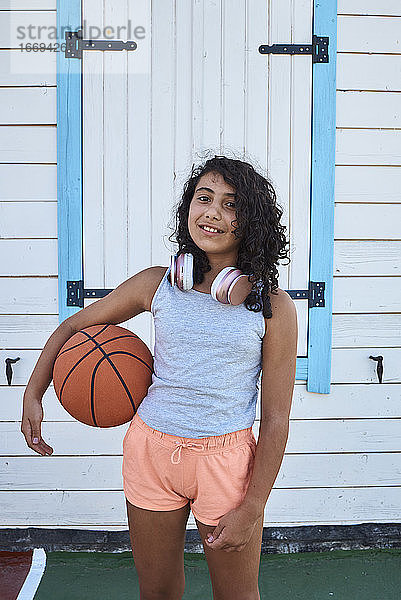 Ein kleines Mädchen mit lockigem Haar  Kopfhörern und einem Basketball