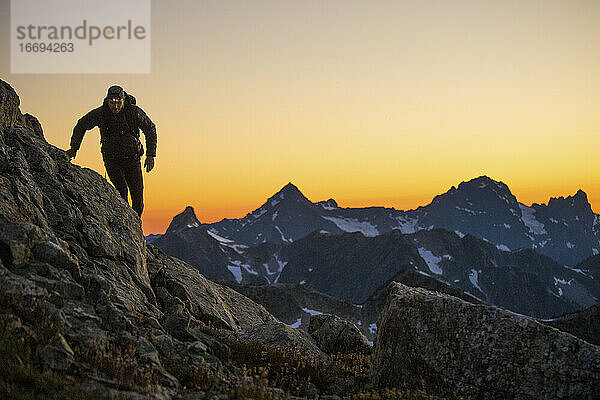 Ein Wanderer geht nach Sonnenuntergang mit einer Stirnlampe einen Bergweg entlang.